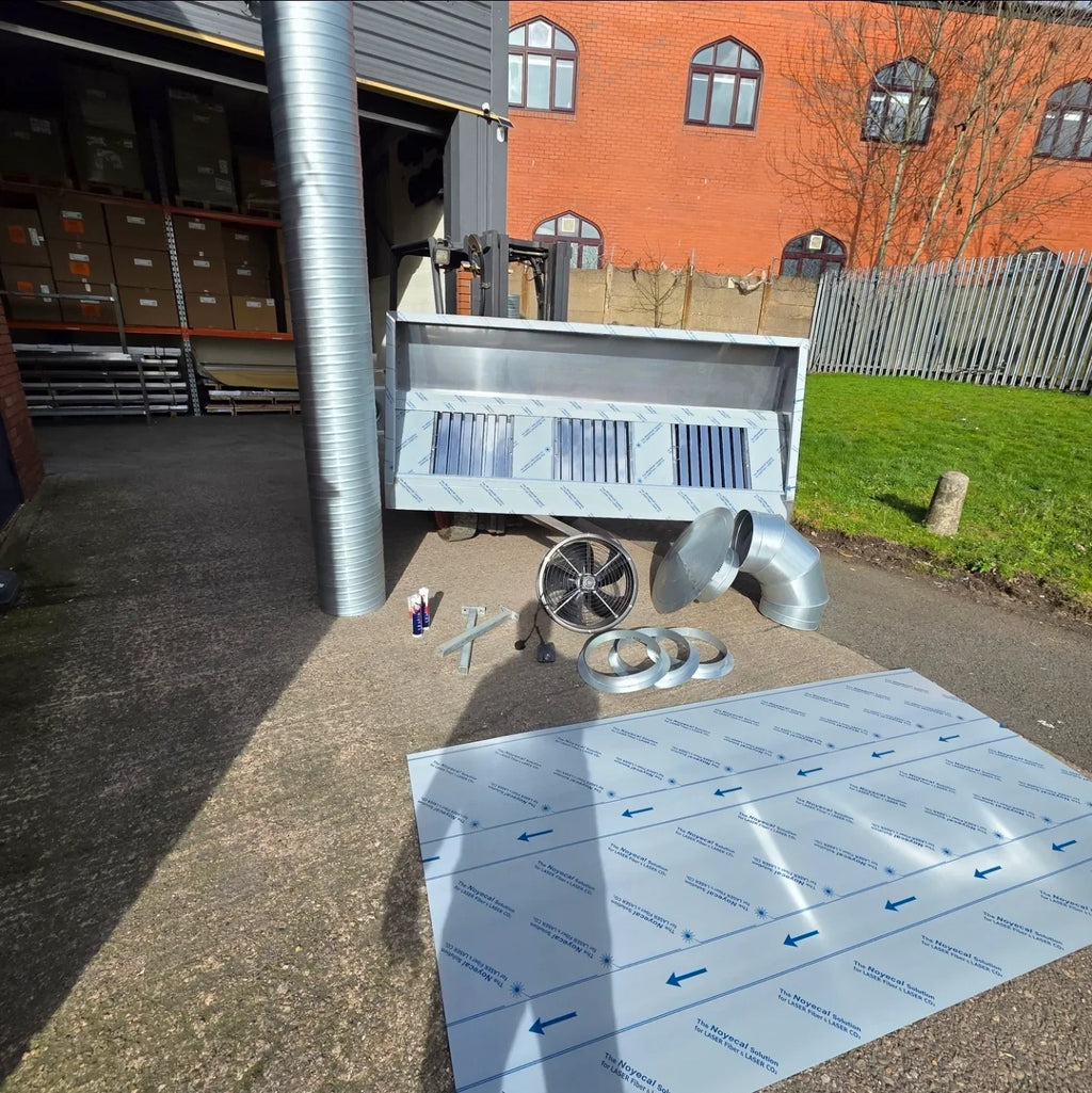 Ventilation system components and ducts on a concrete floor with a building in the background.