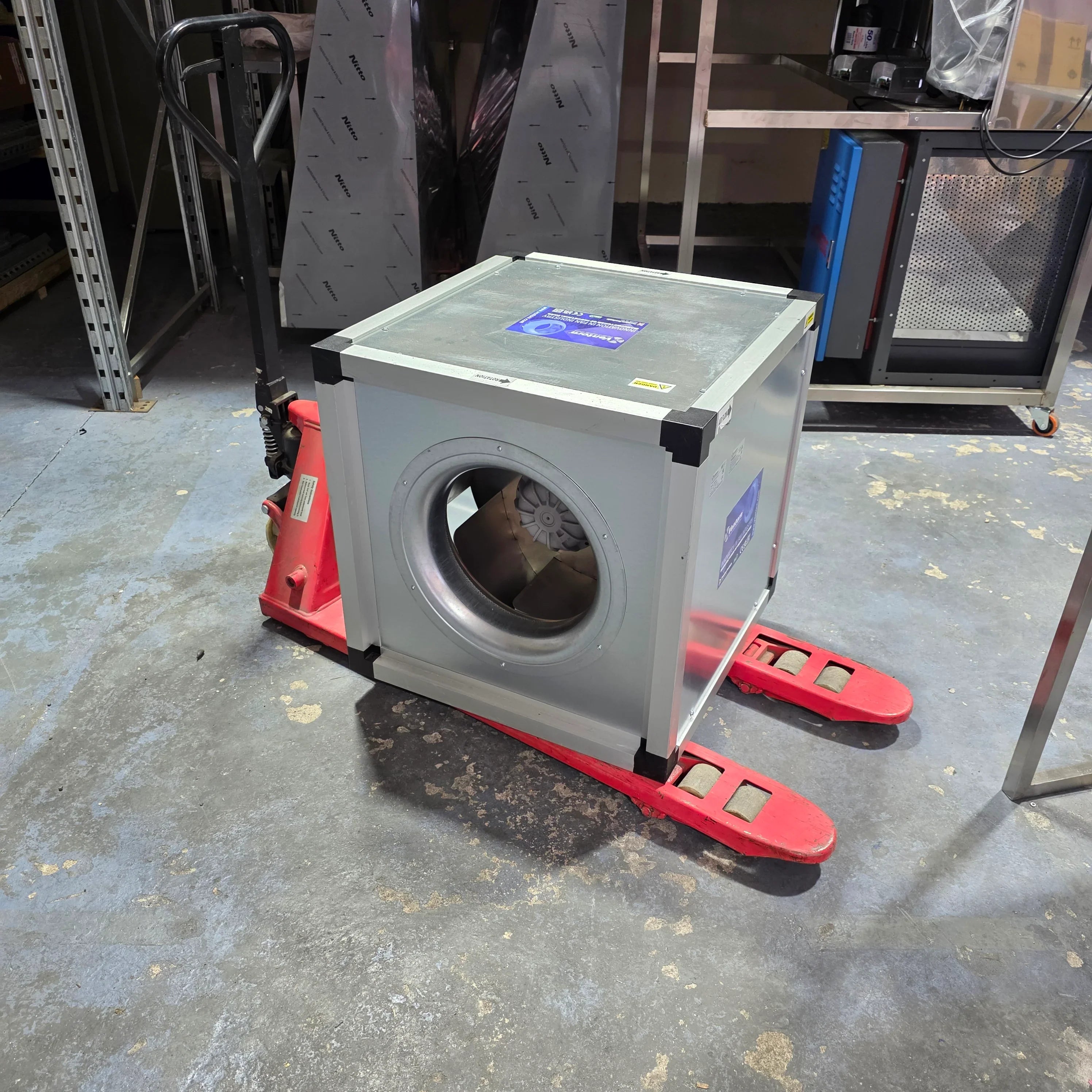 Industrial ventilation fan on red pallet jack in warehouse, metal ducting visible